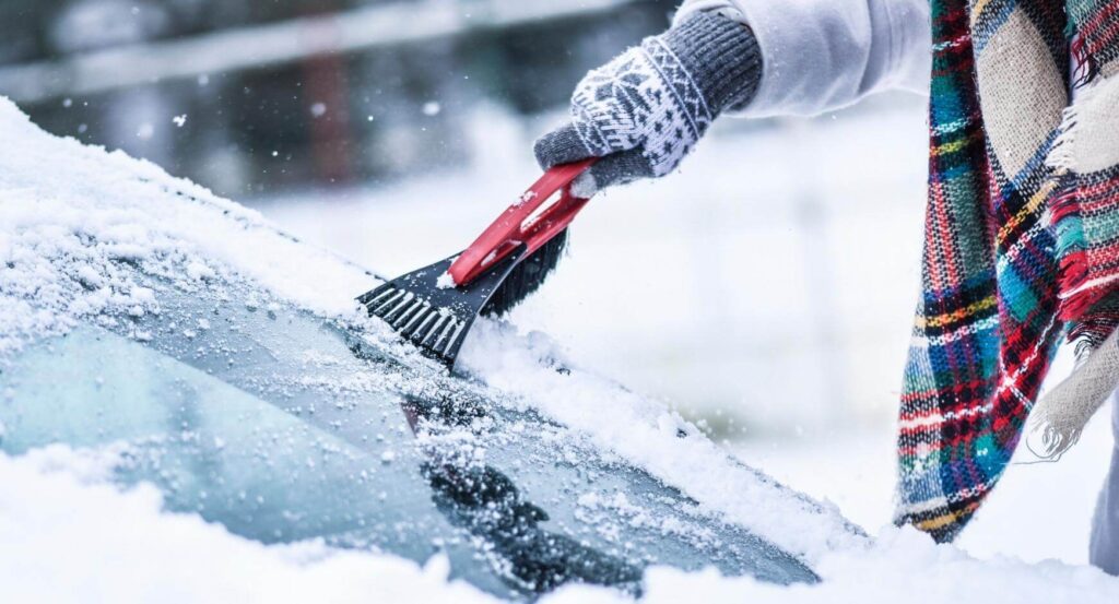 car essentials header image of a person scraping snow off their car